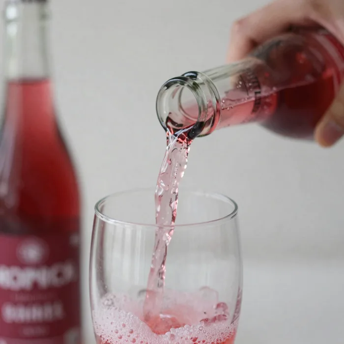 A close-up of a hand pouring cloudy pet-nat into a glass