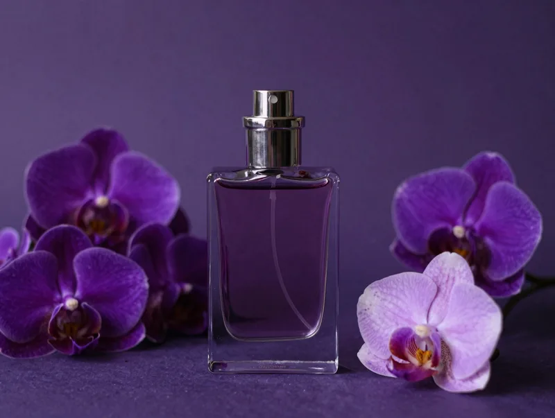 A dark still life of a perfume flacon among night-blooming flowers, deep purple and violet