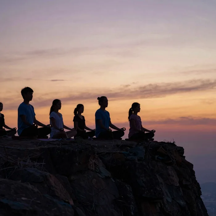 A group meditating on a cliff at sunset, silhouettes against warm sky