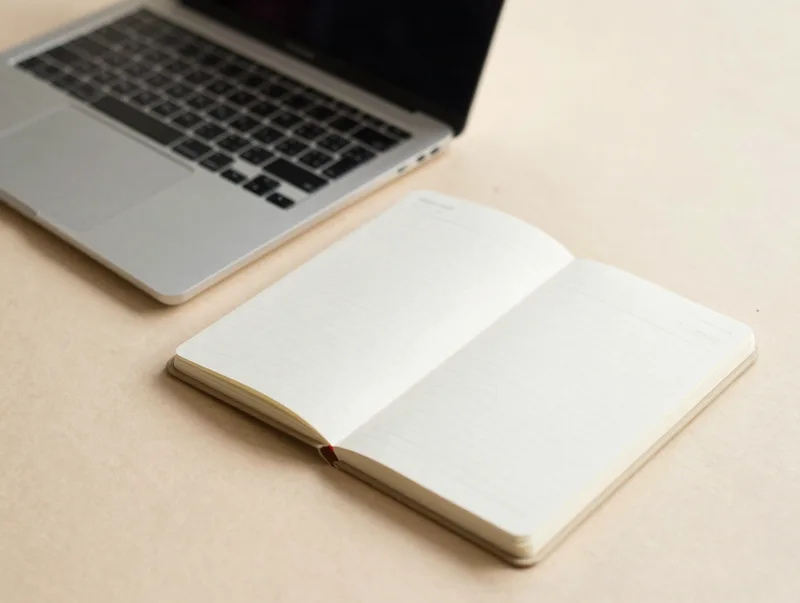 A clean flat-lay of a small laptop and notebook on a warm paper desk, minimal editorial photo
