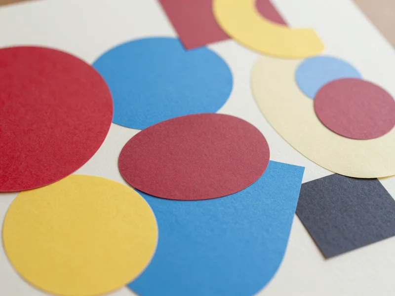 A geometric collage of overlapping paper shapes in red, blue, and yellow, playful print-style artwork