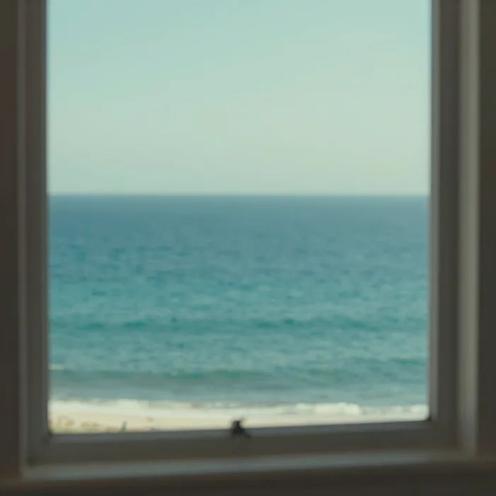 An interior with a large window framing the ocean, soft light
