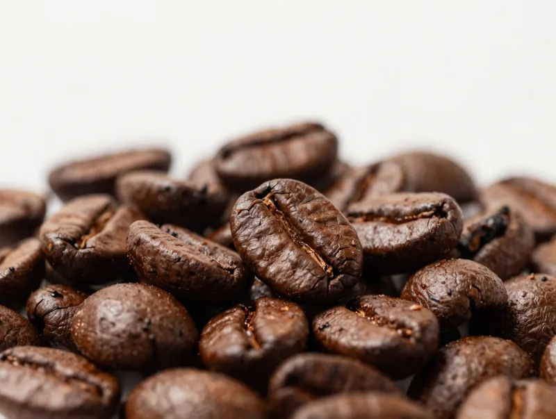 Glossy roasted coffee beans piled close-up with warm highlights, rich brown coffee photography