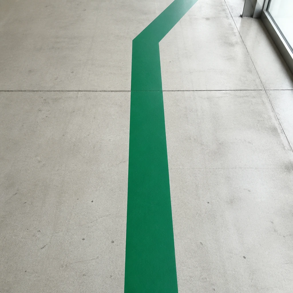 A painted green directional stripe running across a pale concrete floor
