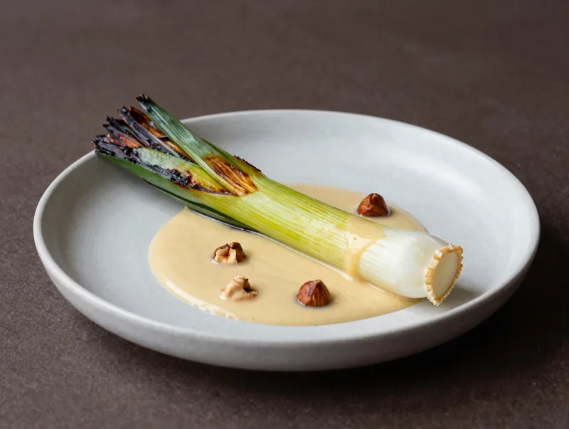 A charred whole leek plated with ember cream and hazelnut, dark moody restaurant lighting